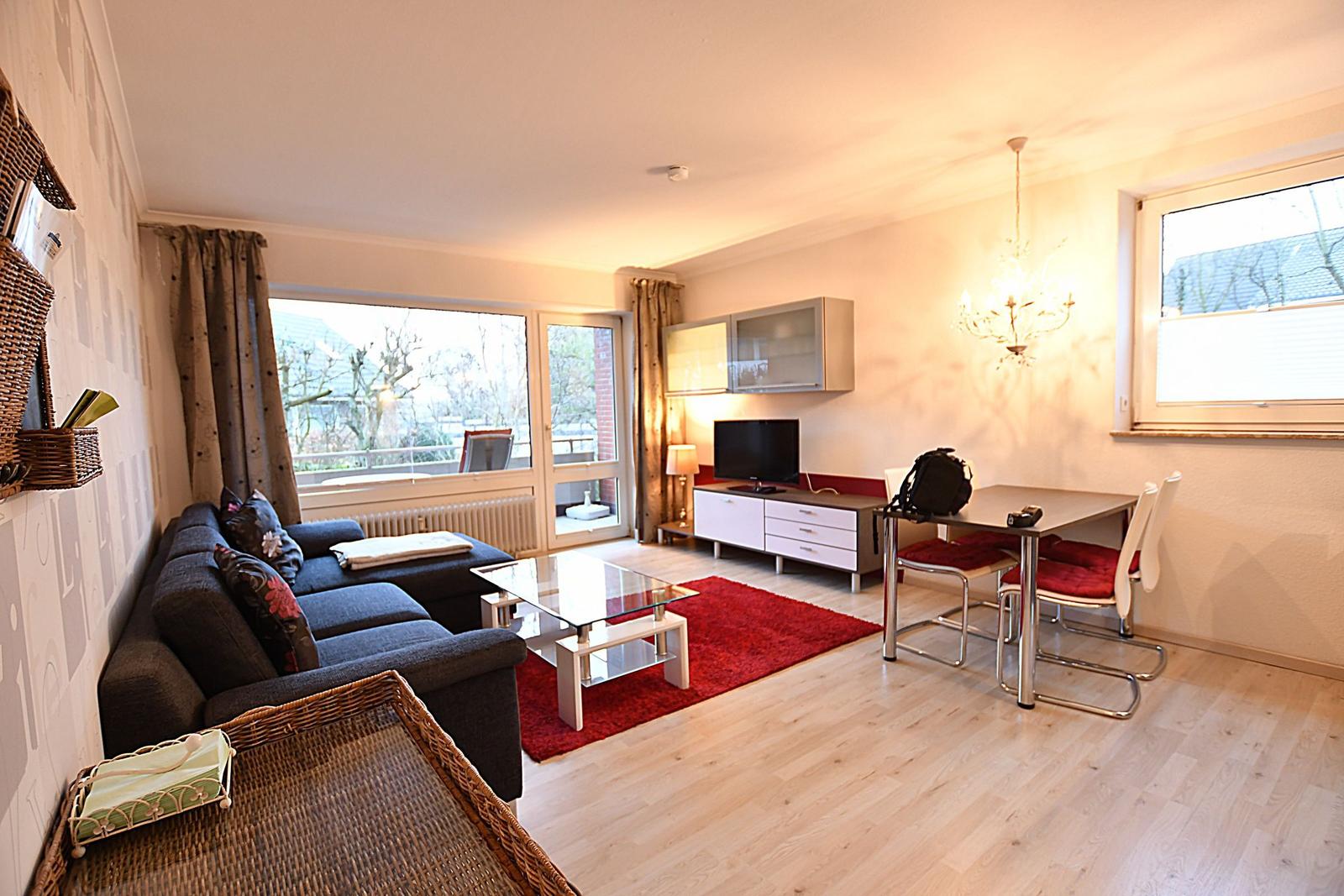 Wohn- und Essbereich mit Sofa, Glas-Tisch und TV. Rote Teppich und Essgruppe.