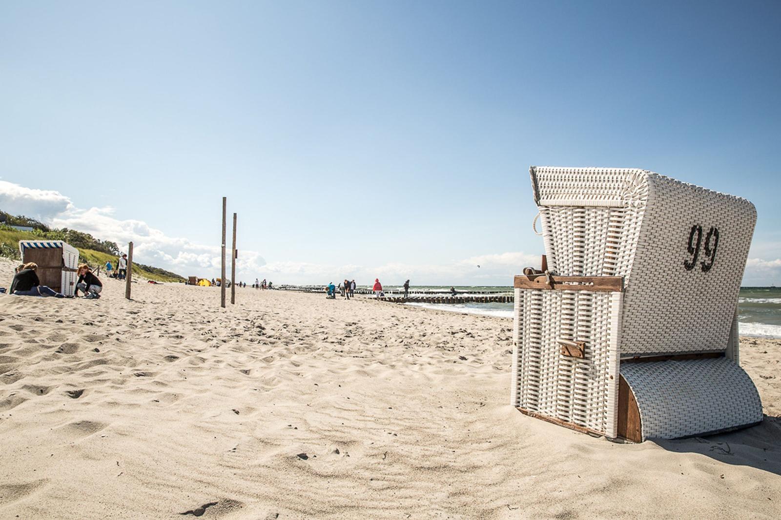 Weißer Strandkorb mit der Nummer 99 auf sandigem Strand.