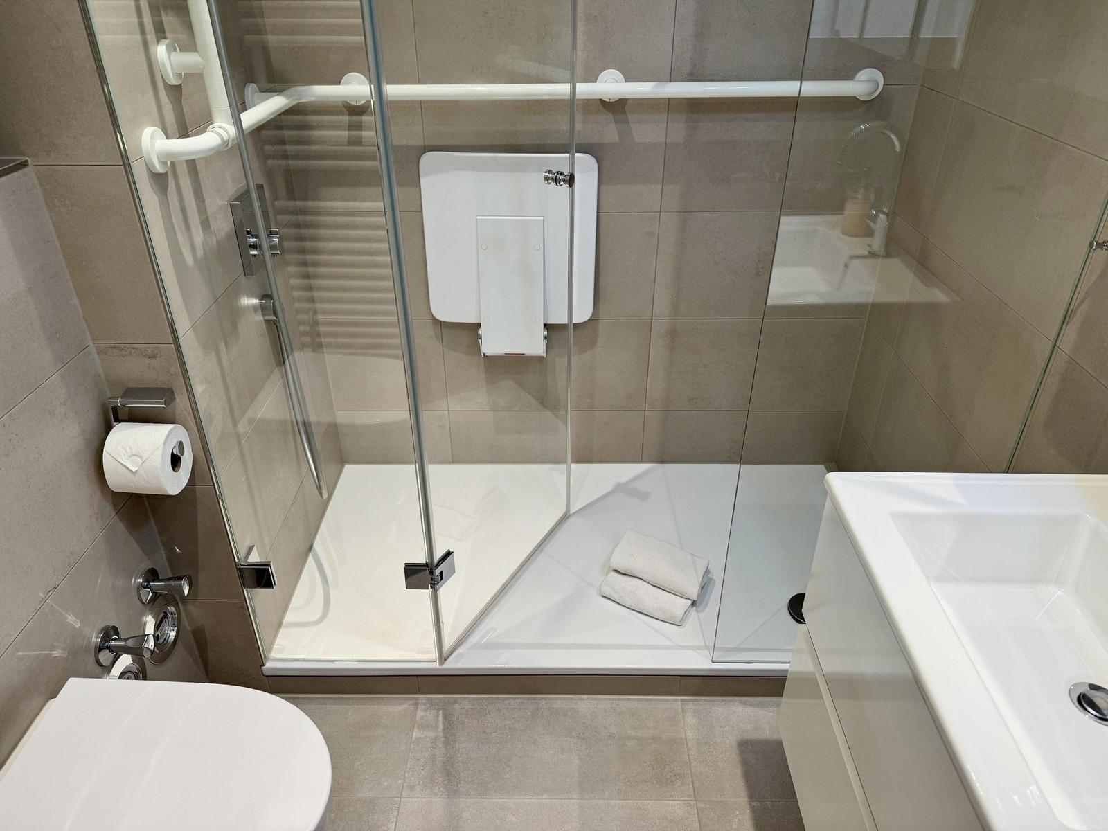 Duschbad mit Rollstuhlgerechter Dusche, Toilette und Waschbecken.