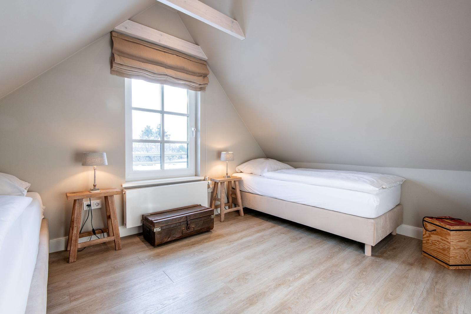 Zimmer mit zwei Betten, Holzboden und Dachschrägen. Fenster mit Rollladen und Nachttische.