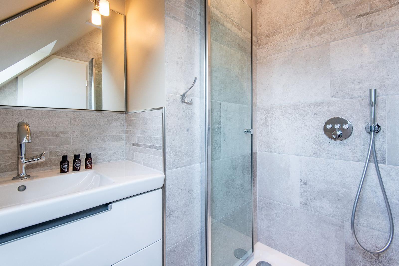 Badezimmer mit Dusche und Waschbecken. Fliesenwand, Spiegel und Duschbrause.