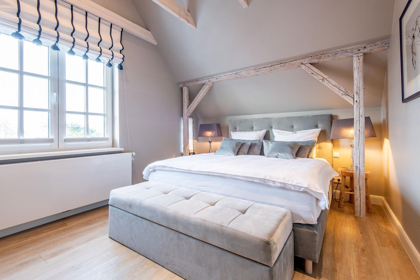 Schlafzimmer mit großem Bett, Holzbalken und Fenster mit Rollladen.