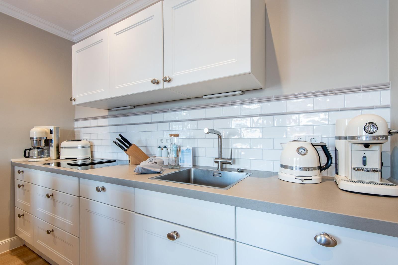 Küche mit weißen Schränken, Edelstahlspüle und Küchengeräten auf Arbeitsfläche.