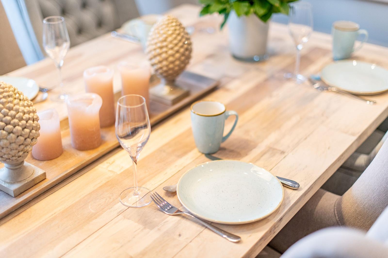 Holztisch mit Gedeck, Gläsern und Kerzen für gemütliche Mahlzeiten.