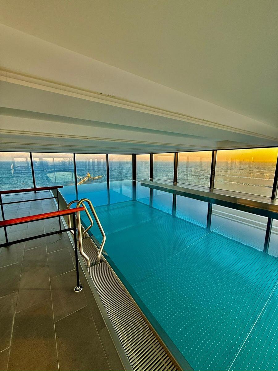 Innenpool mit Meerblick und Sonnenuntergang durch große Fenster.