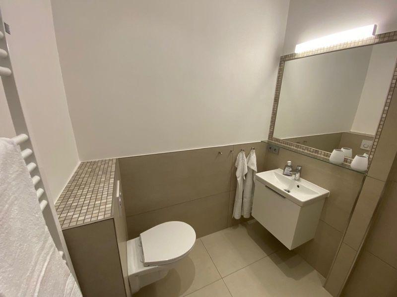 Badezimmer mit Toilette, Waschbecken und Spiegel. Handtuchhalter und Fliesen sichtbar.