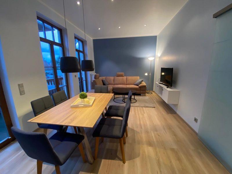 Wohn- und Essbereich mit Holzboden, Sofa, TV und Tisch mit Stühlen.
