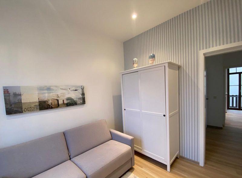 Wohnzimmer mit Sofa, Kleiderschrank und Wandbild. Durchgang zur Terrasse.