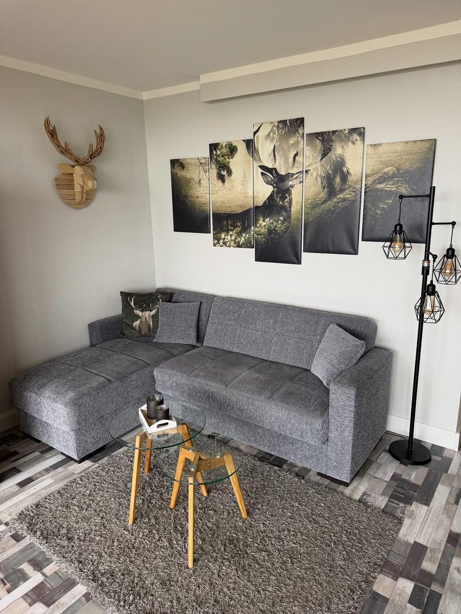 Ein Wohnzimmer mit grauem Sofa, Wandbildern und Holzdekor.