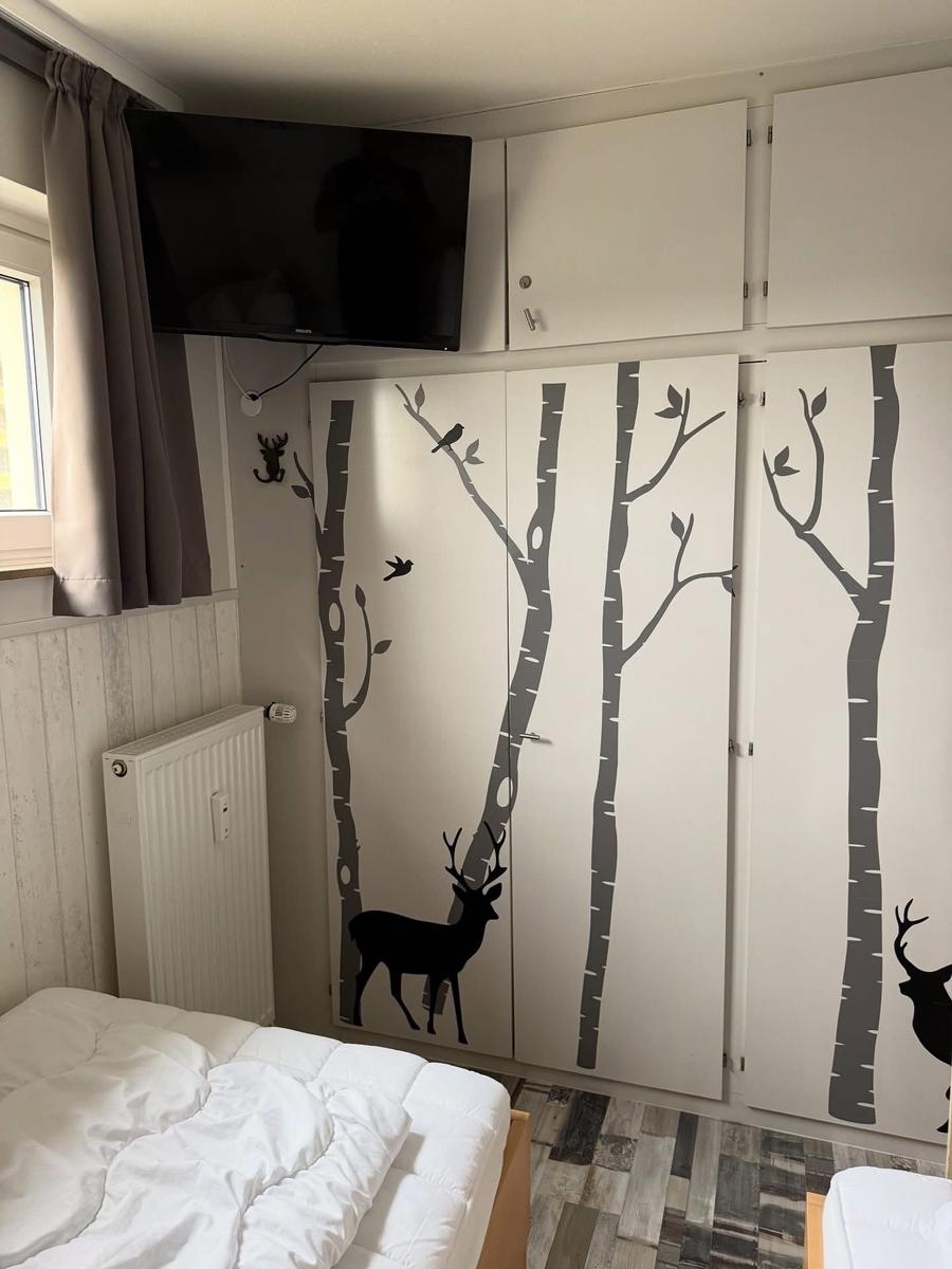 Schlafzimmer mit Bett, TV und Schrank mit Bäumen und Hirschmotiven.