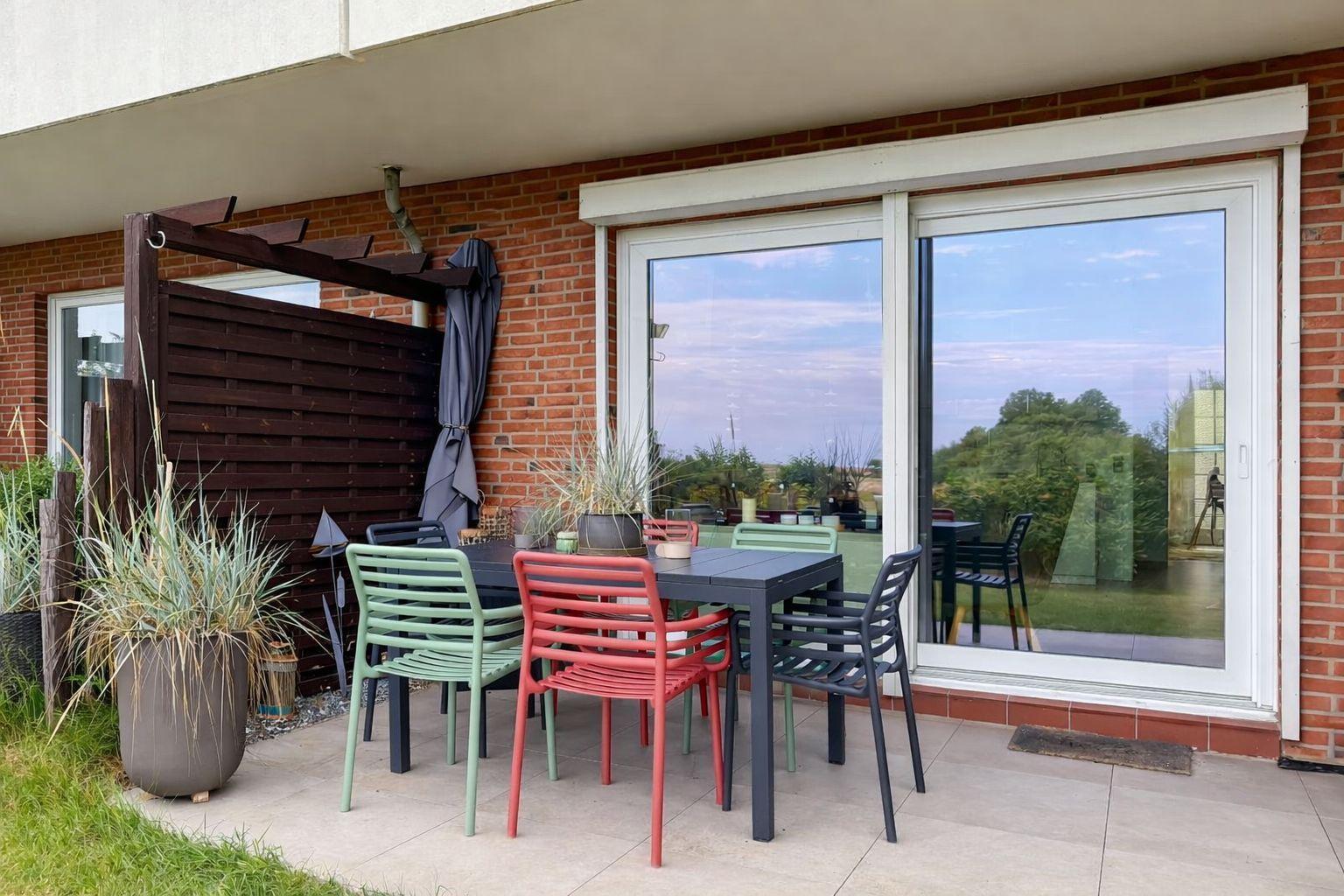 Terrasse mit Tisch und Stühlen, Pergola und Pflanzen vor einer Glasfront.