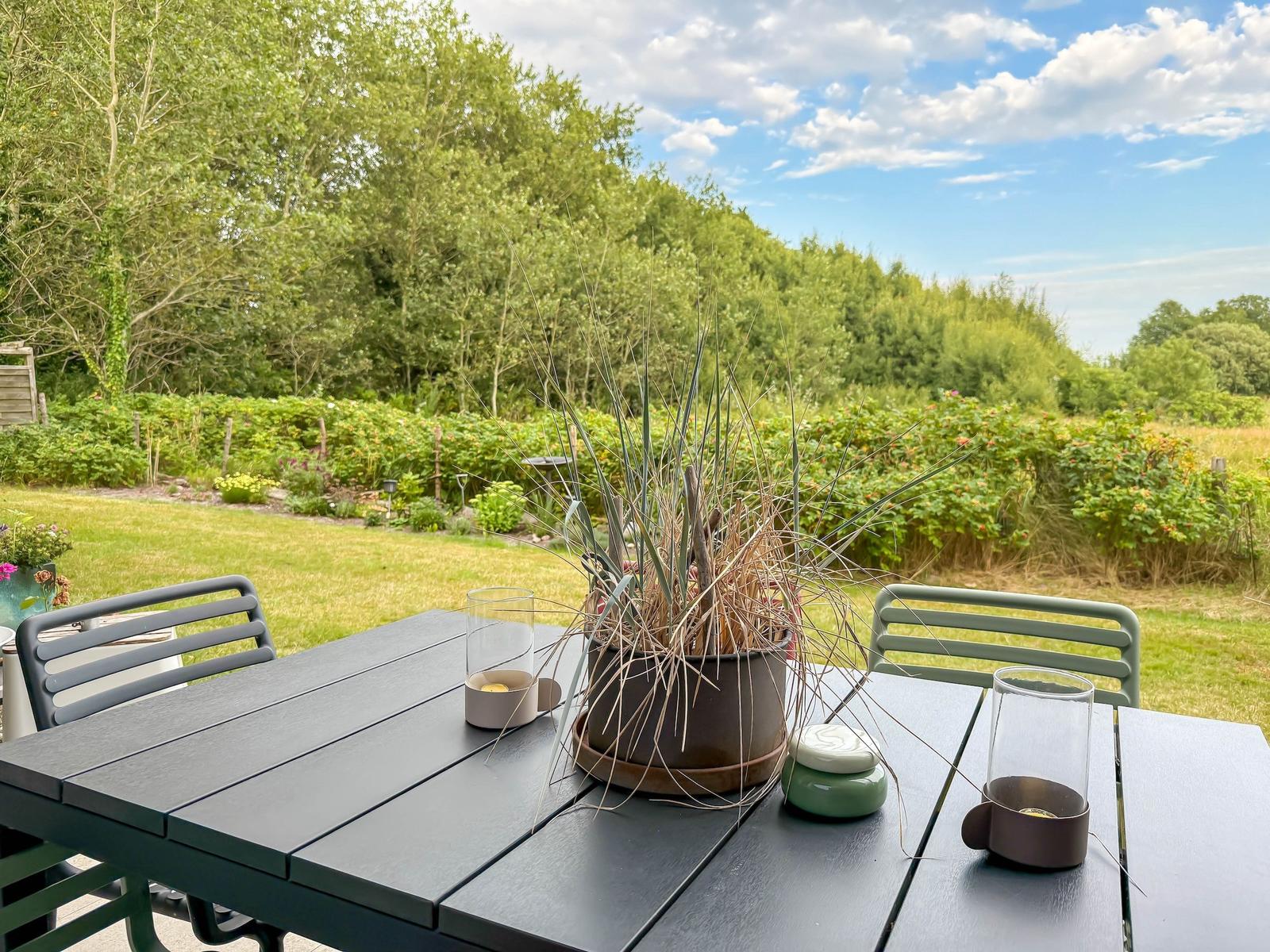 Helle Außenterrasse mit Tisch und Stühlen, Blick auf grünen Garten und Bäume.
