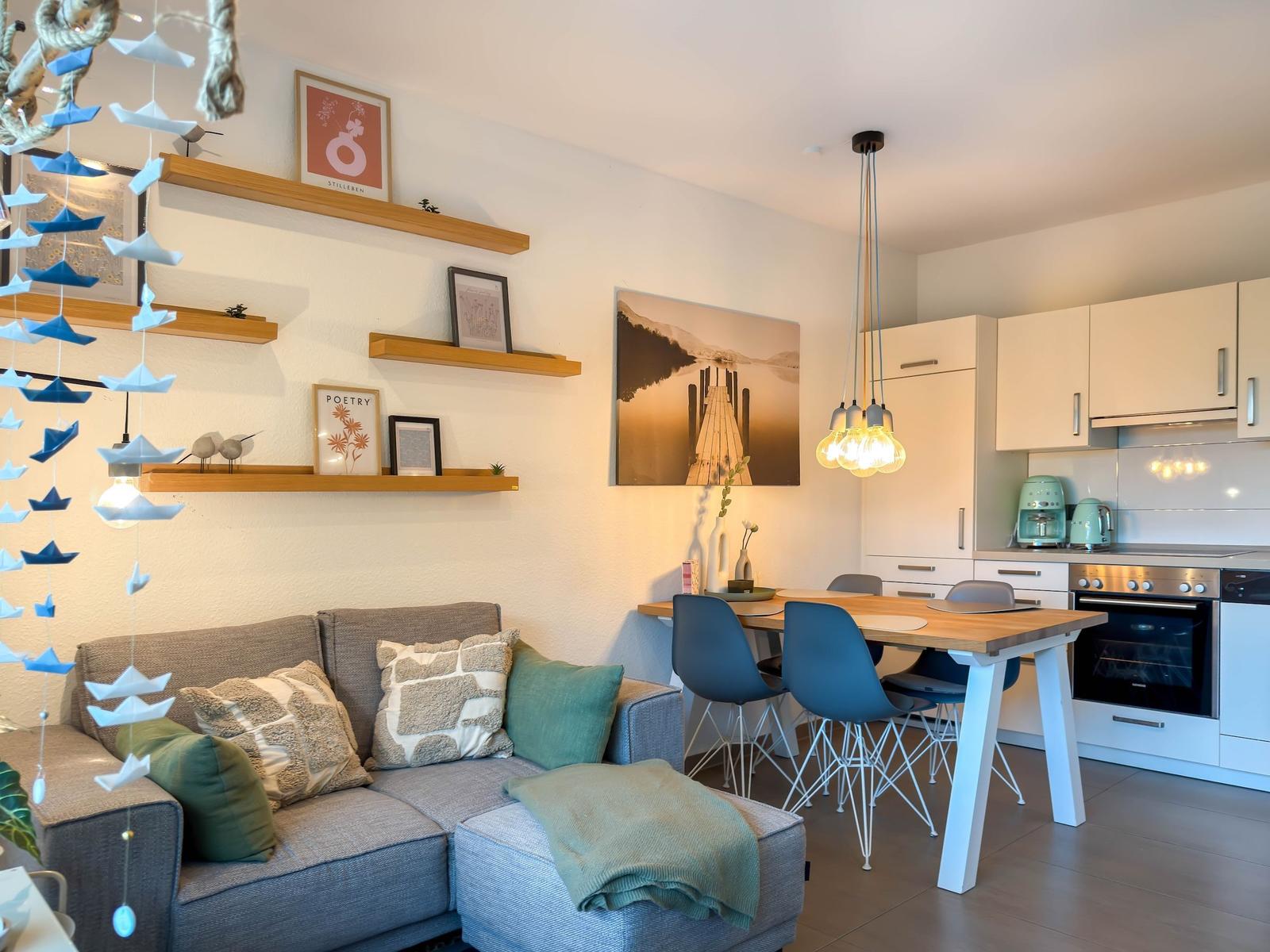 Wohnbereich mit Sofa, Esstisch und Küche. Wandregale, Bilder und Dekoration.