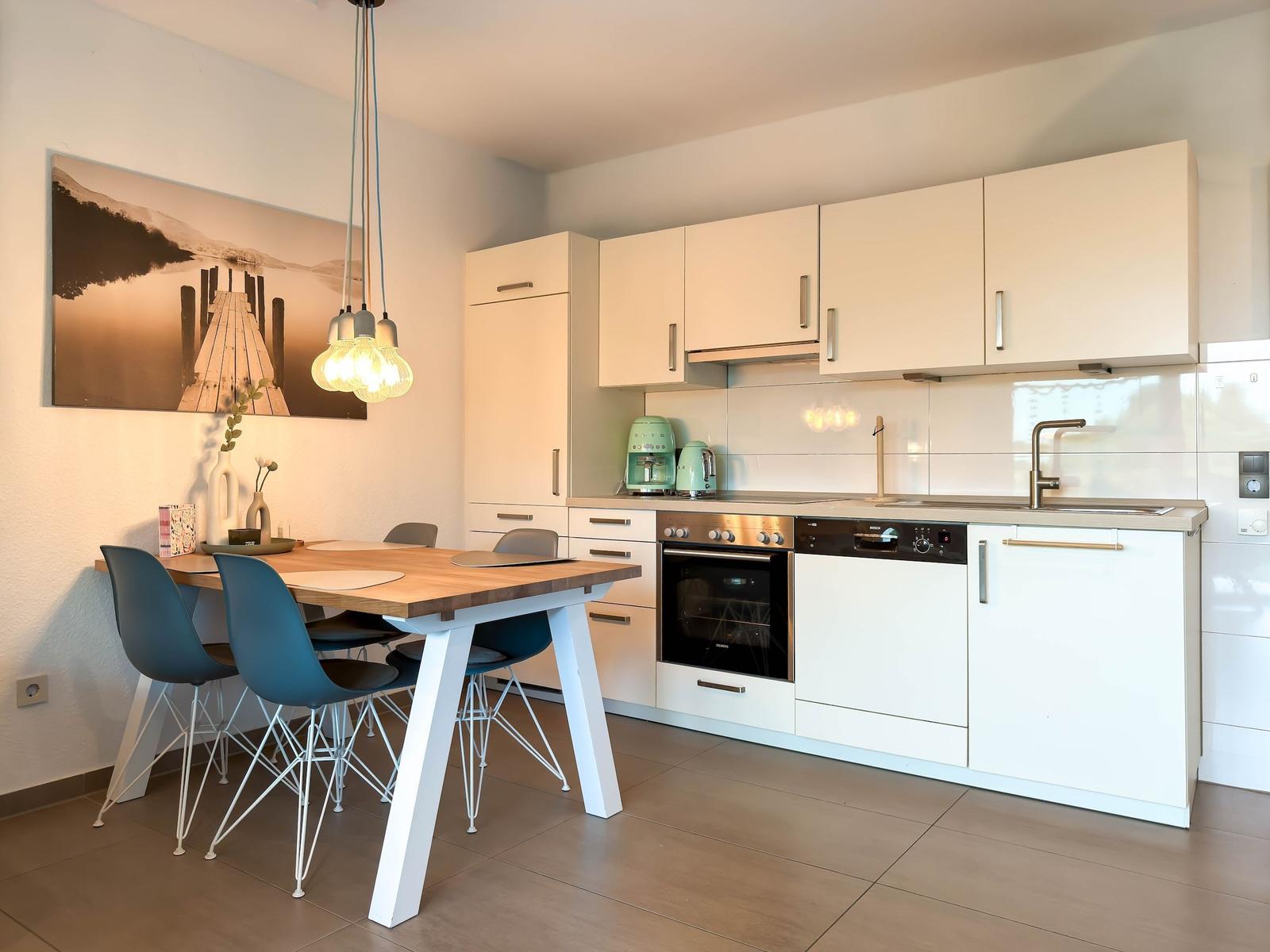 Küche mit Essbereich, weißen Schränken und Holztisch mit blauen Stühlen.