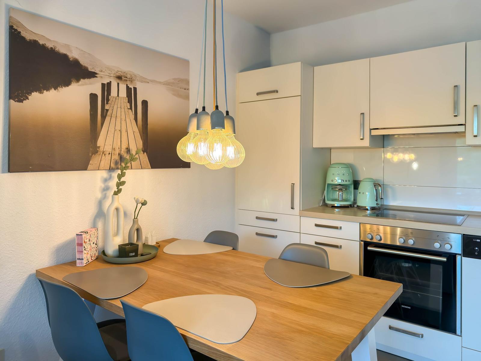 Küche mit Essbereich, weißen Schränken und Holztisch mit Stühlen.