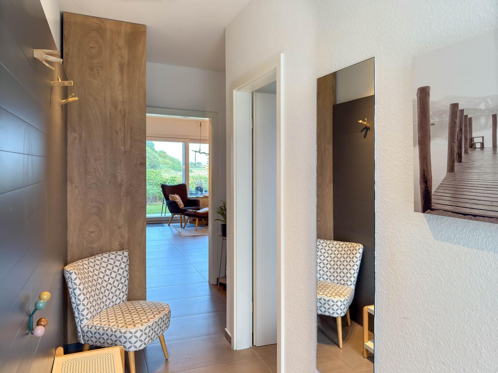Flur mit Stuhl, Spiegel und Wandbild. Durchgang in Wohnbereich mit Sitzgelegenheit.