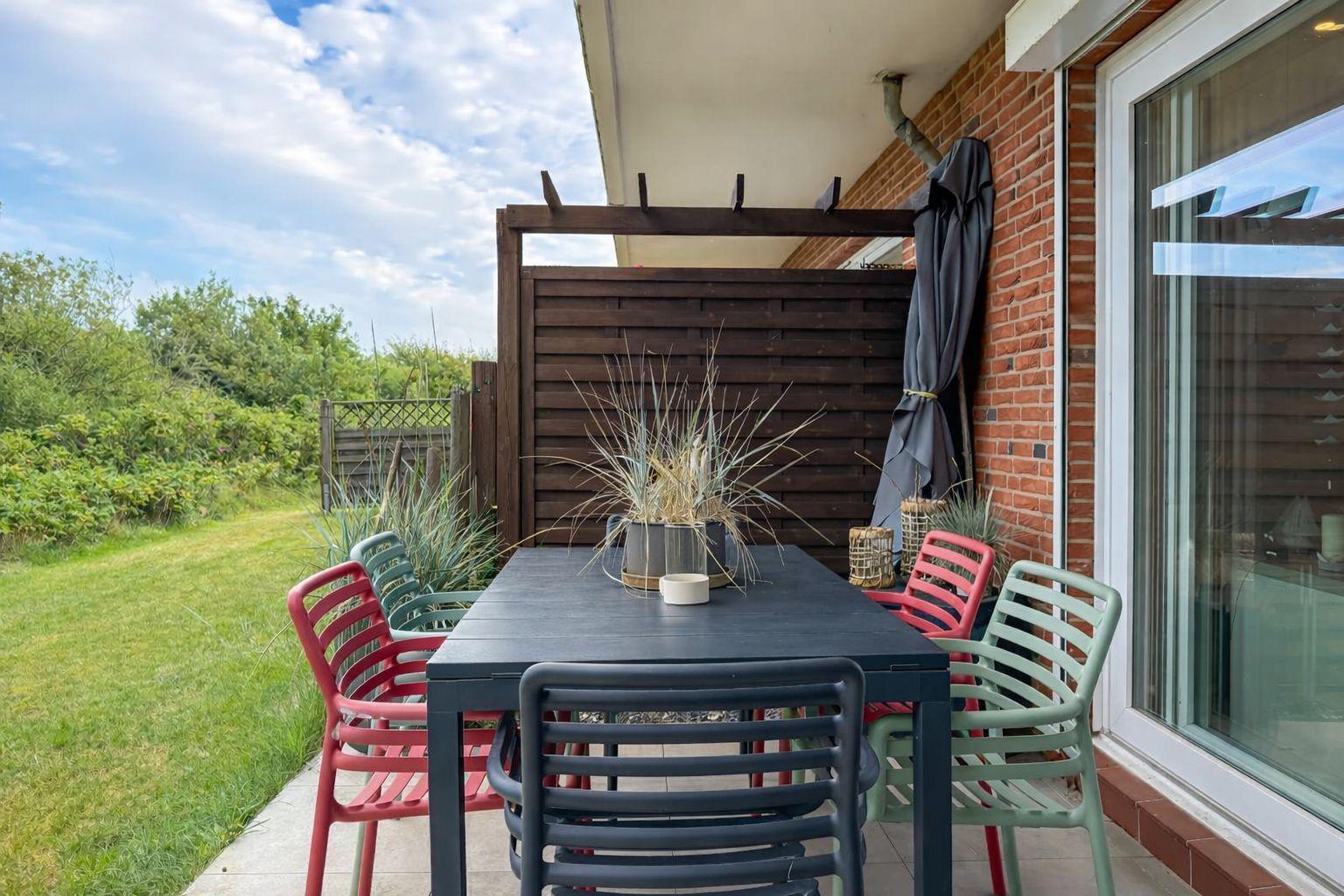 Terrasse mit Tisch und Stühlen, Sicht auf Grünflächen und Holzgeländer.