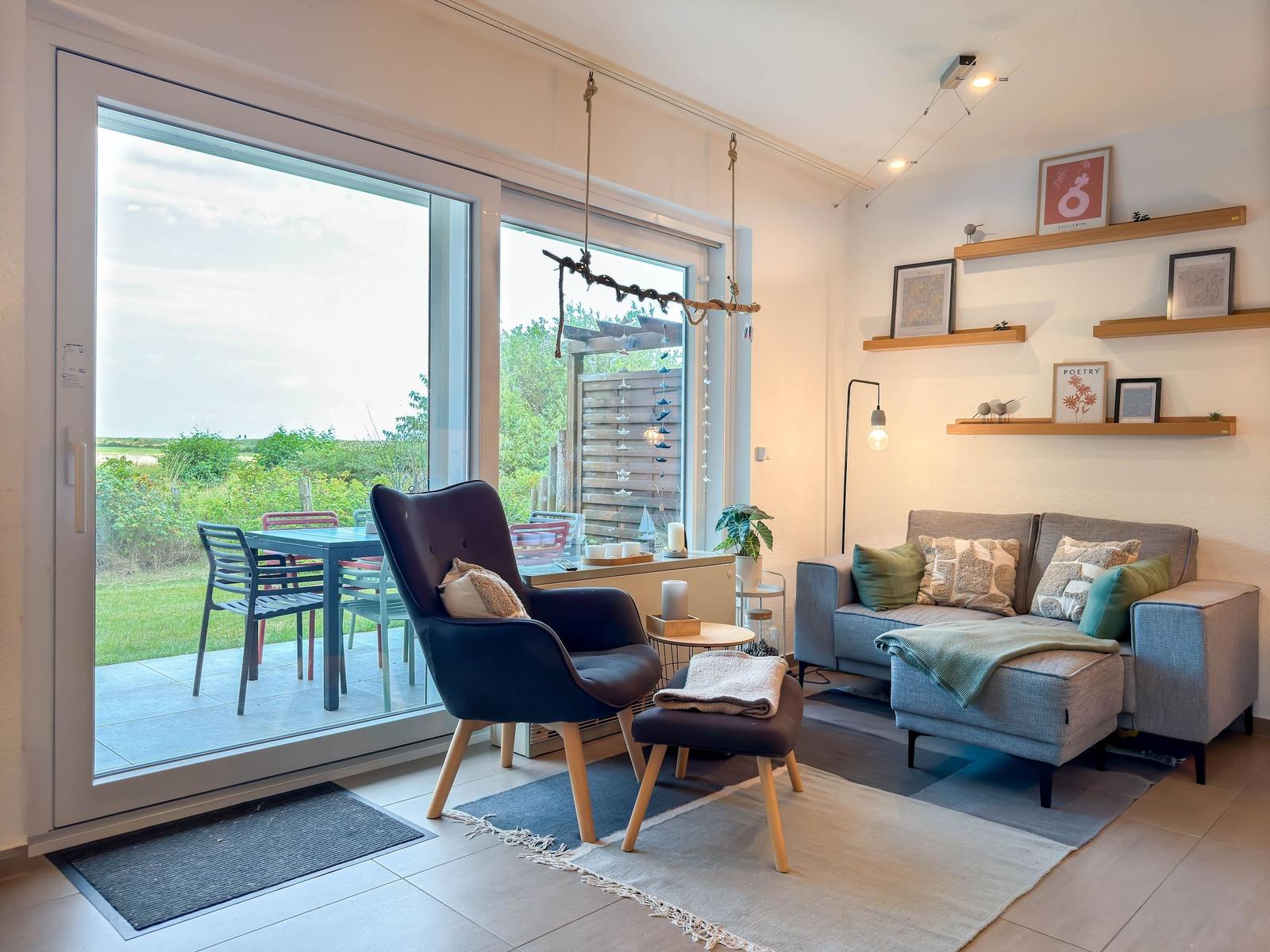 Wohnzimmer mit Sofa, Sessel und Terrasse mit Tisch und Stühlen.