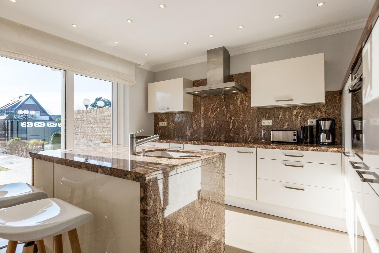 Moderne Küche mit Edelstahlspüle, Marmorarbeitsplatte und Blick auf Garten.