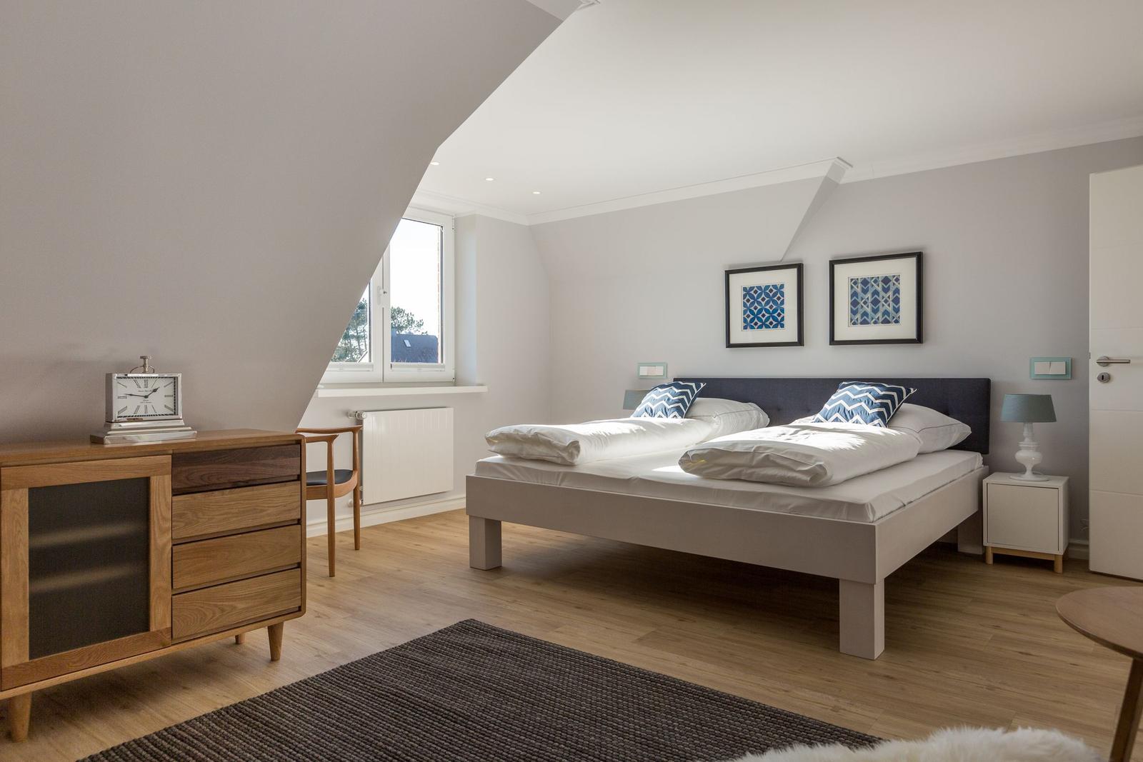 Schlafzimmer mit Doppelbett, Nachttisch, Schrank und Fenster. Decke ist schräg.