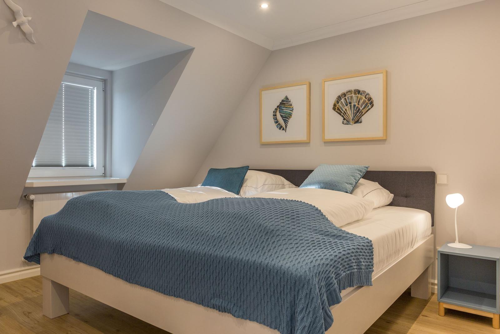 Schlafzimmer mit Dachschrägen, Bett mit blauer Decke und zwei Bildern an der Wand.