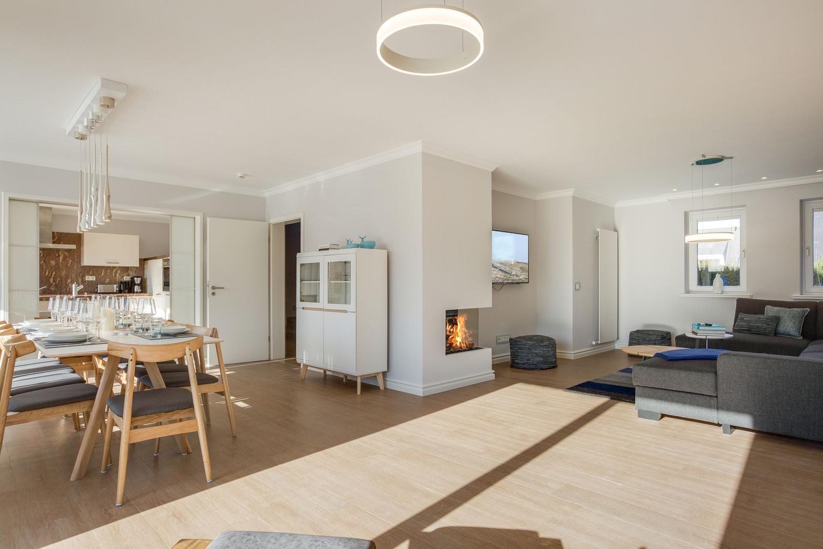 Wohn- und Essbereich mit Kamin, Sofa und Esstisch. Holzboden und moderne Beleuchtung.