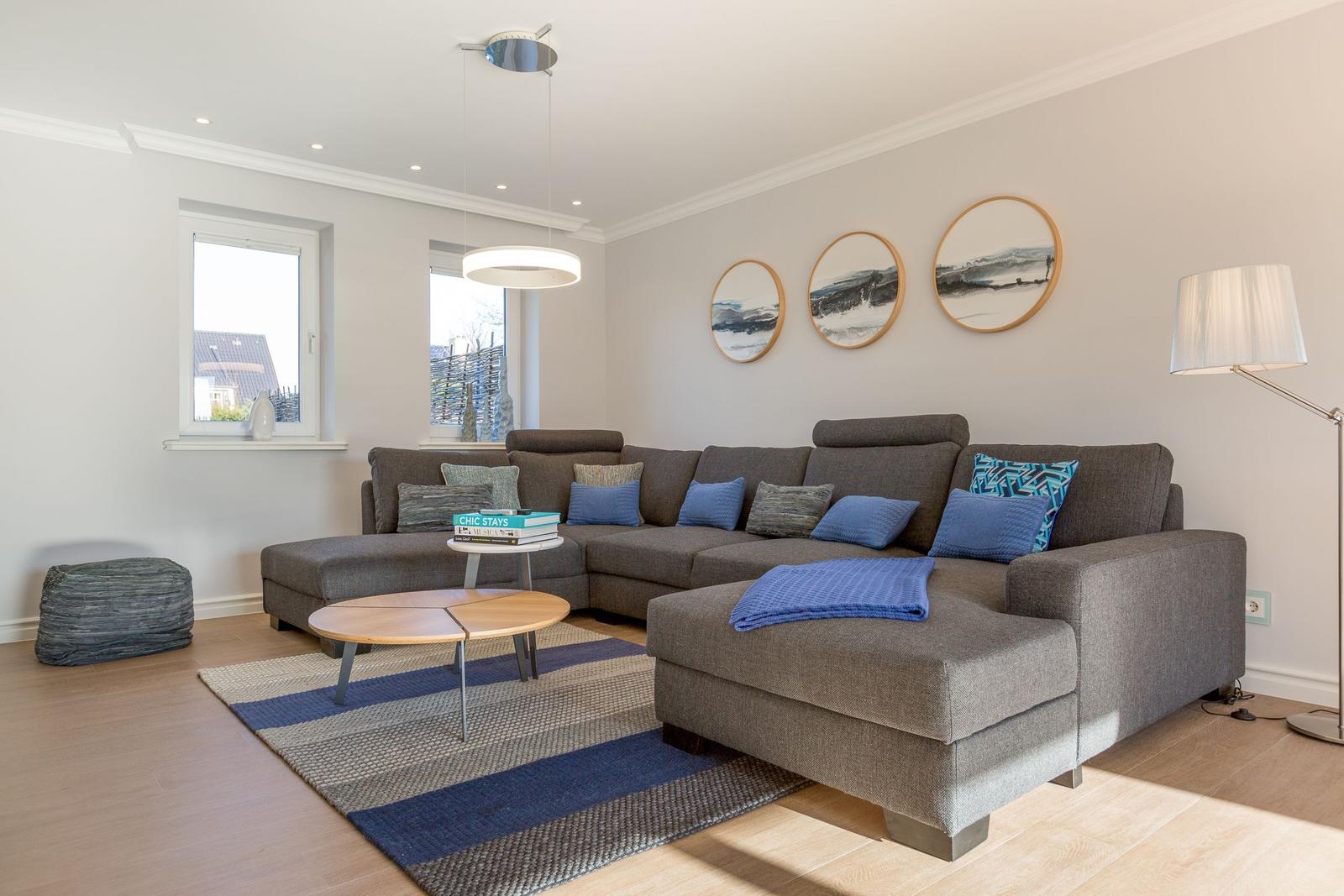 Ein Wohnzimmer mit grauem Sofa, blauen Kissen und einem runden Tisch.