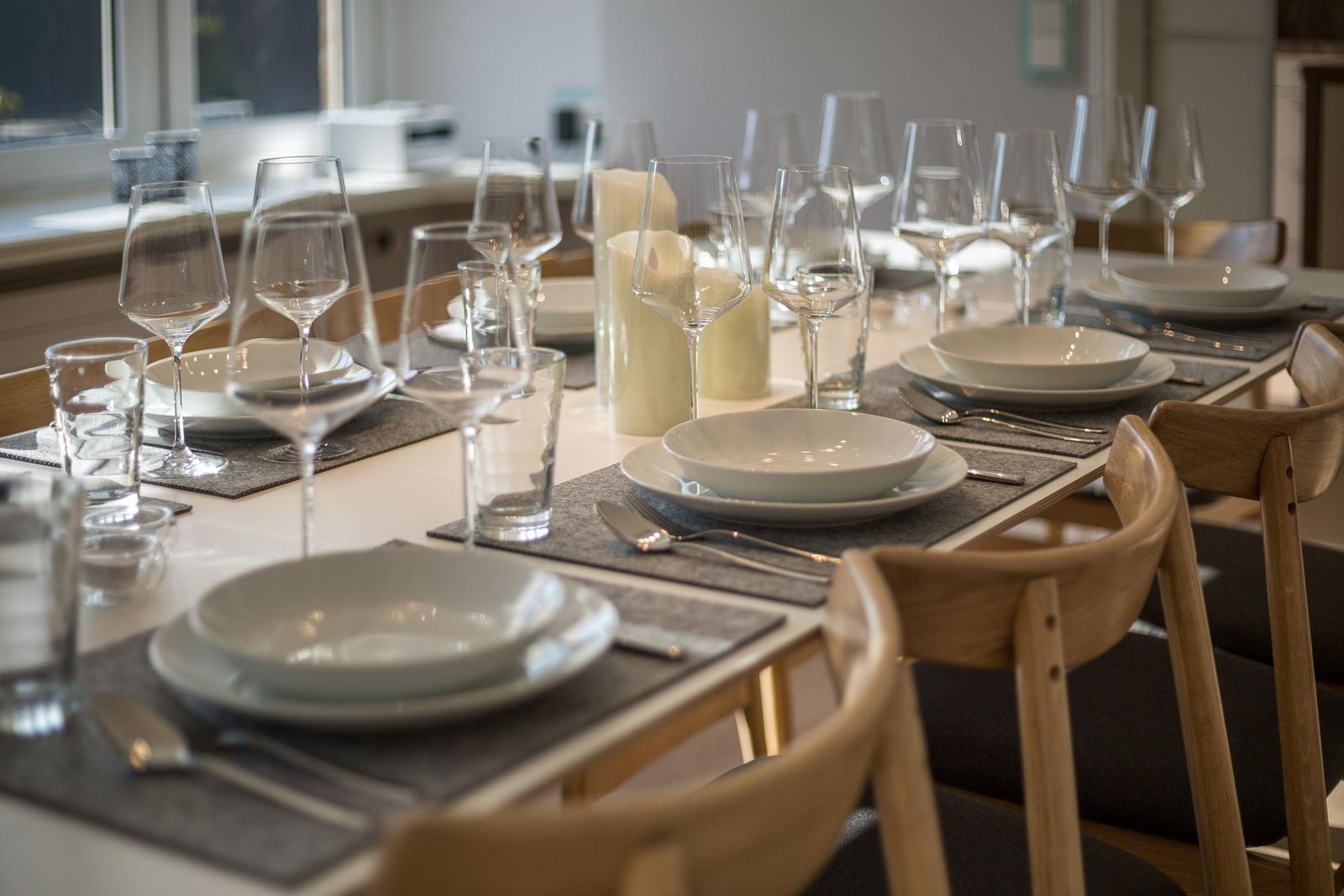 Esstisch mit Tischdecken, Tellern, Gläsern und Stühlen.