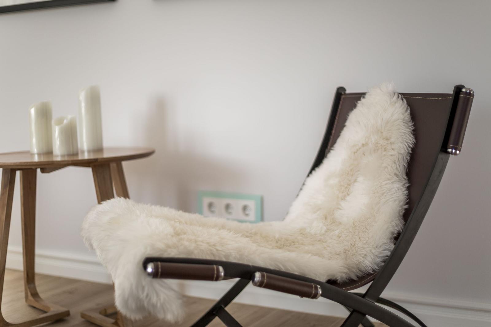 Ein Stuhl mit weißem Fellbezug steht neben einem Holztisch mit Kerzen.
