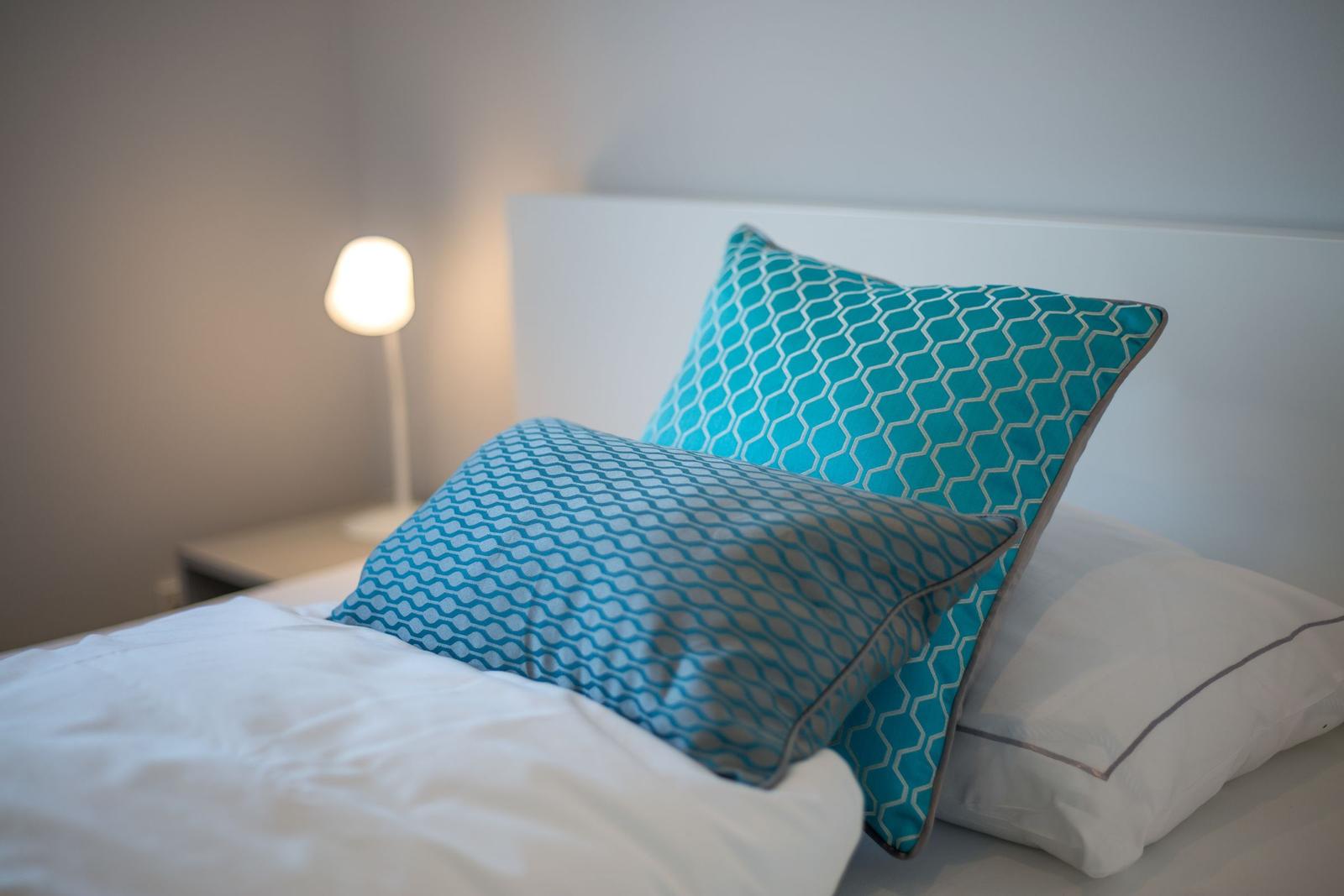 Ein Bett mit weißen Laken und zwei blauen Kissen mit Muster.