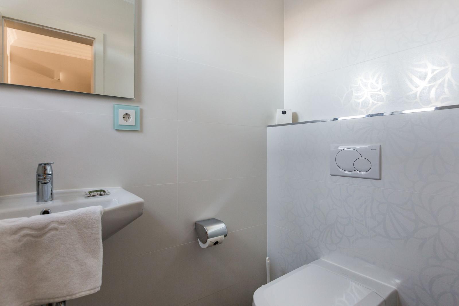 Badezimmer mit Waschbecken, Spiegel und Toilette. Wandfliesen mit floraler Musterung.