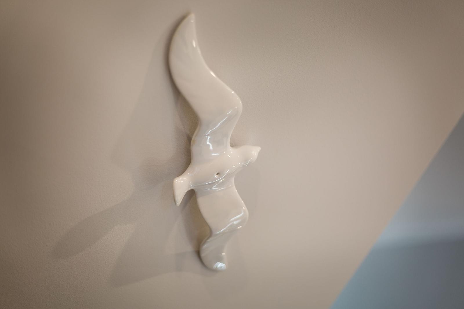 Eine weiße Vogelskulptur an der Wand hängt.