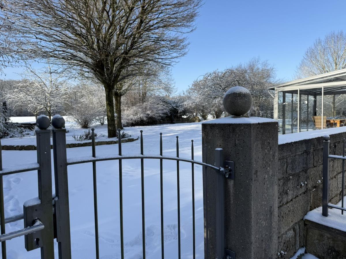 Schneebedeckter Garten mit Zaun und Terrasse im Hintergrund.
