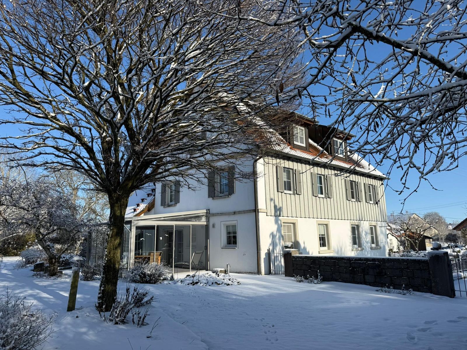Schneefreie Terrasse mit Sitzgelegenheiten vor einem zweistöckigen Haus mit Holzfassade.
