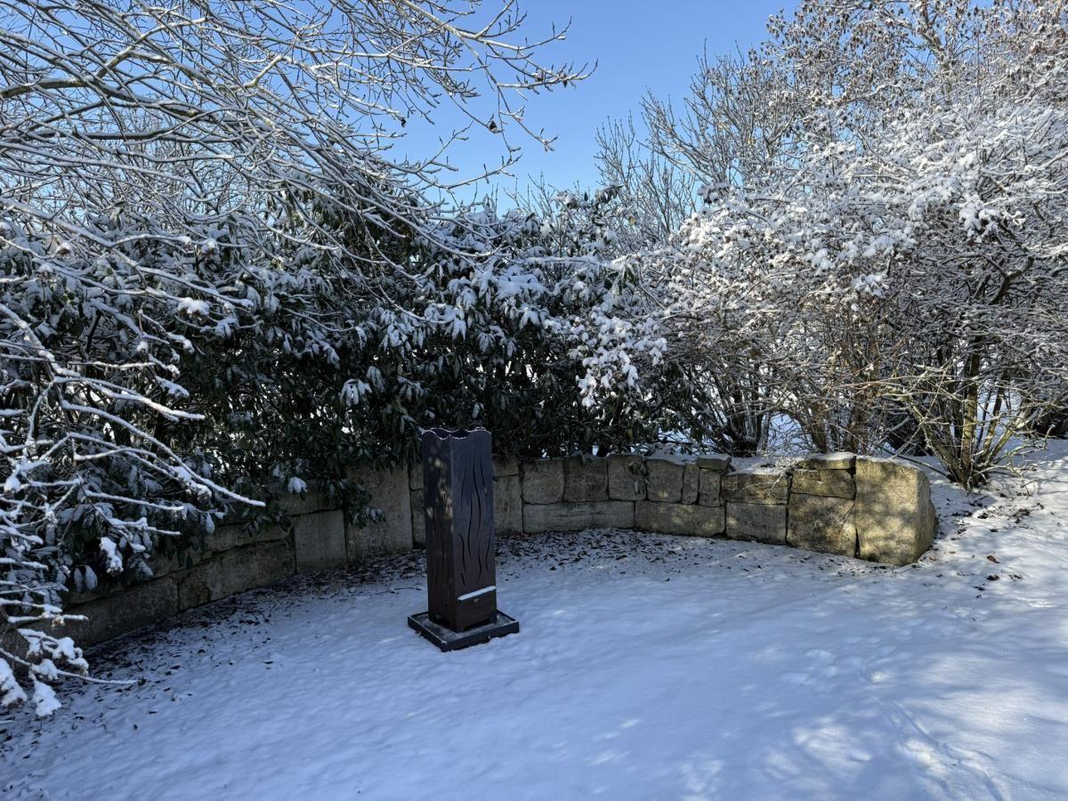Schnee bedeckt einen Garten mit Steinmauer und einer dunklen Skulptur.