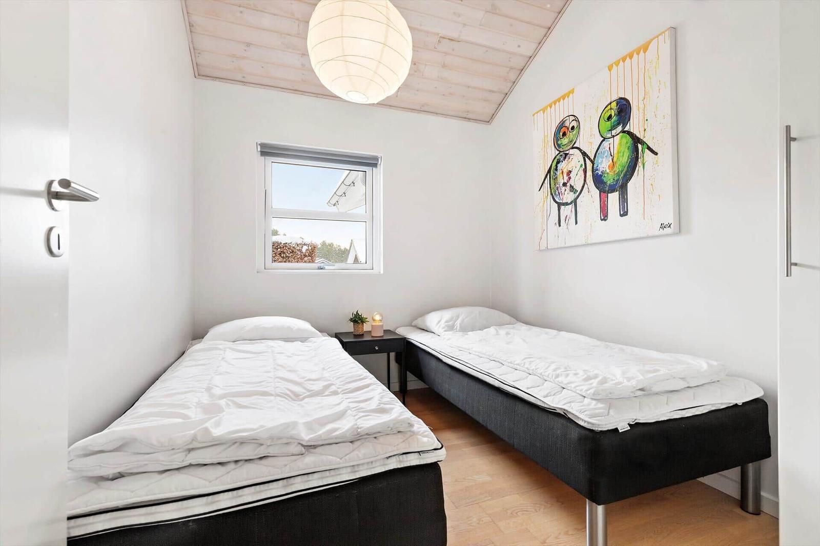 Two single beds, window, wall art, and ceiling lamp in a bedroom.