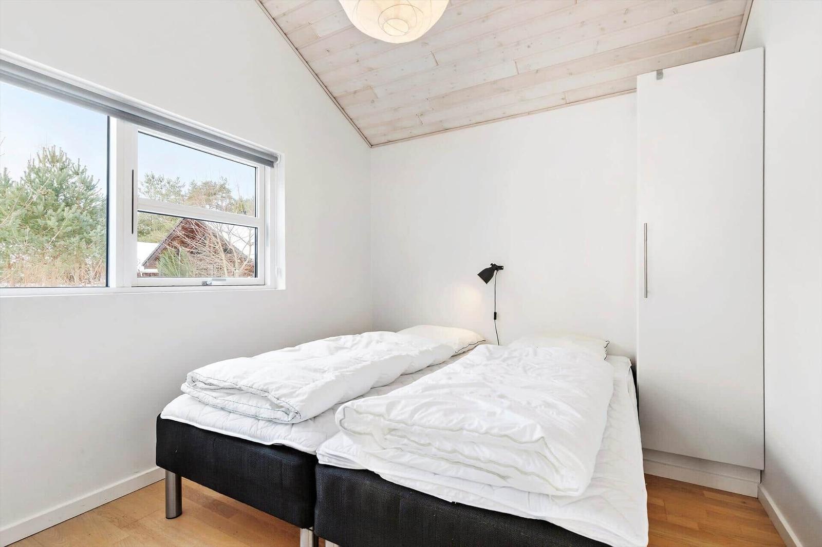 Room with double bed, window, and wardrobe. Wooden ceiling and floor.