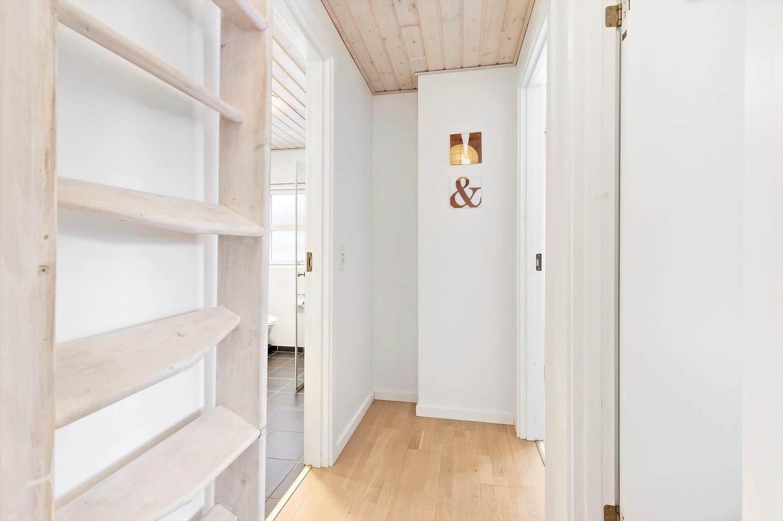 Hallway with wooden ceiling, white walls, and hardwood floor. An ampersand sign hangs on the wall.