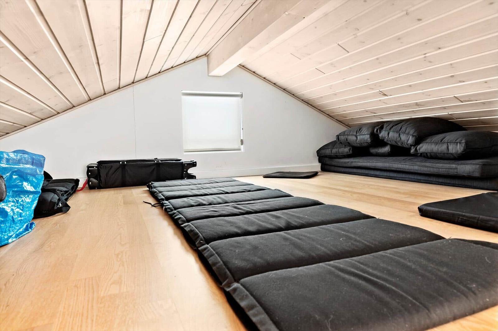 Attic room with mattresses and pillows on wooden floor under wooden ceiling