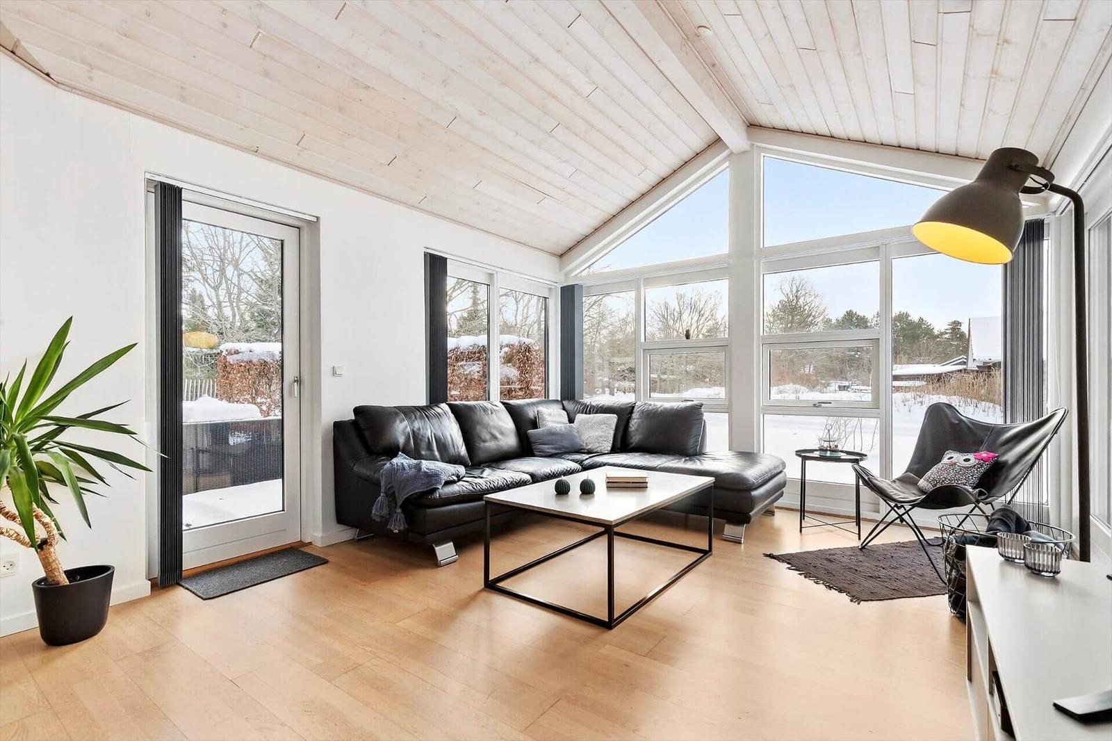 Living room with black leather sofa, large windows and wooden floor. Snow outside.