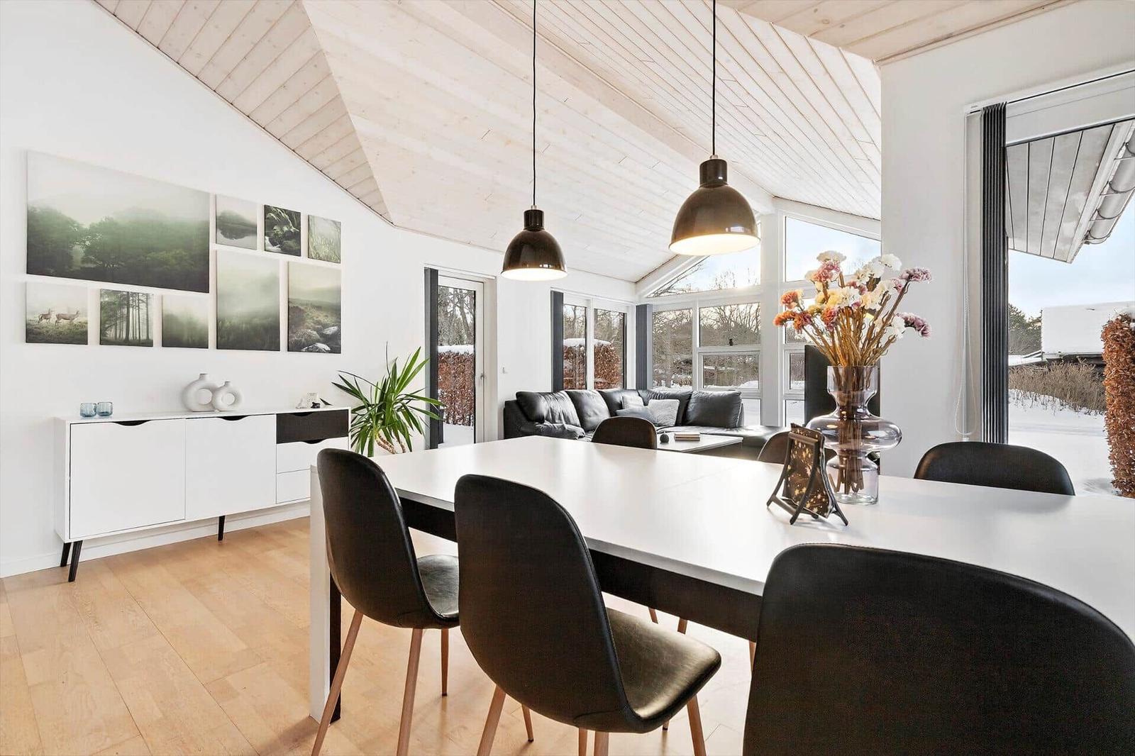Dining area with white table, black chairs, and large window view. Light wood ceiling and wall art.