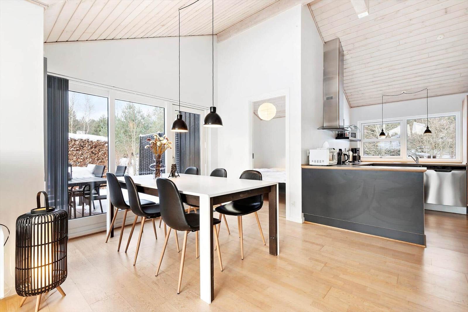 Dining area with table and chairs, kitchen with countertop and windows.