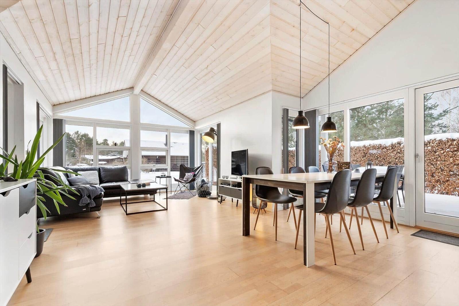 Living and dining area with wooden ceiling, large windows, and modern furniture.