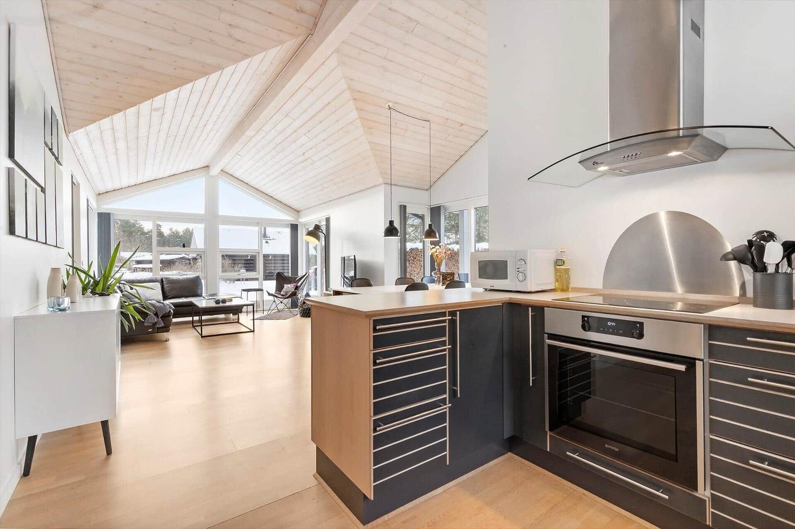 Kitchen with stainless steel appliances and wood surfaces. Living area with sofa and large windows.
