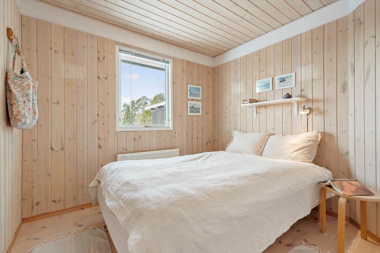 A bedroom with wooden walls, a bed, and a window.