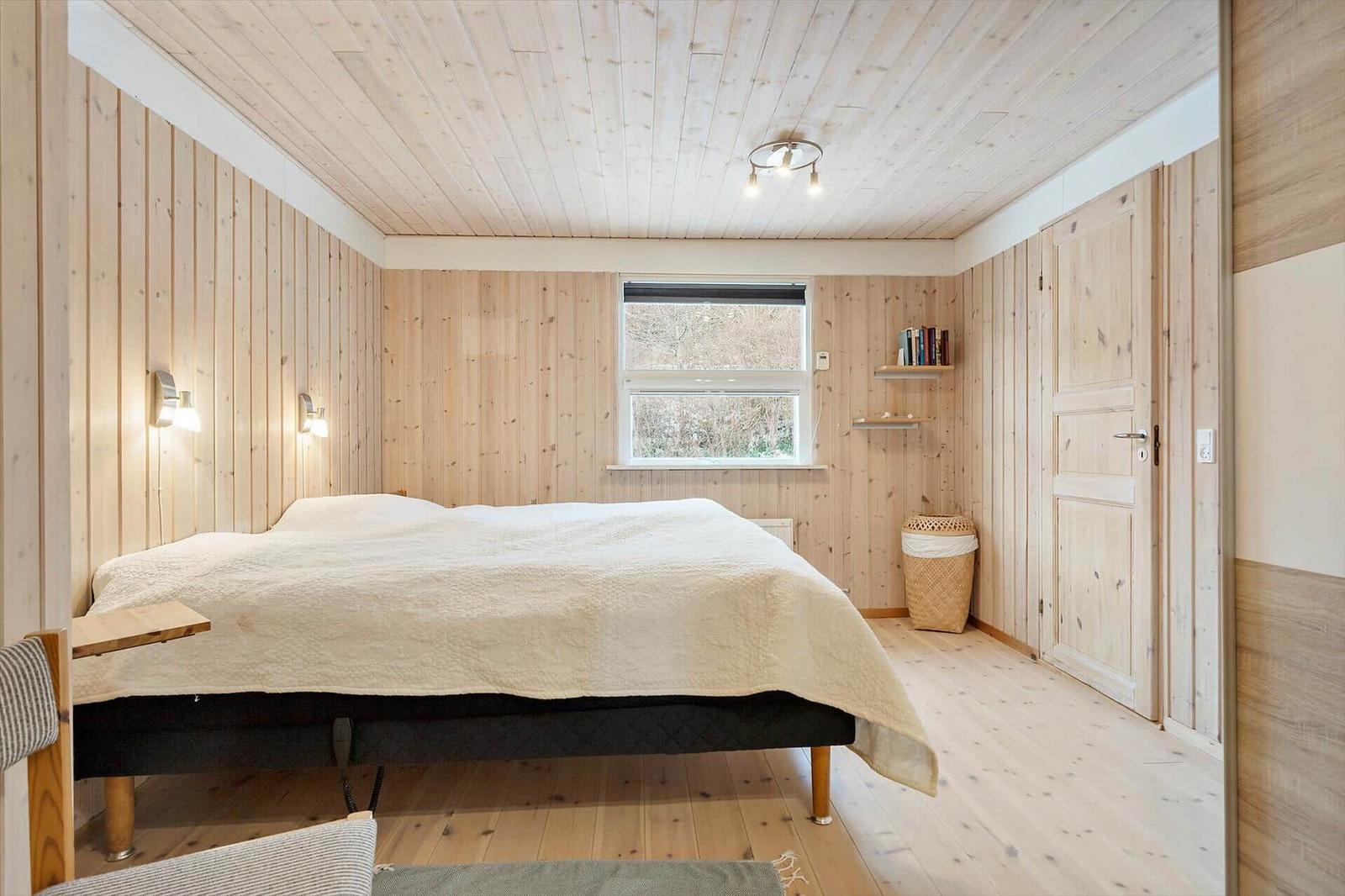 Bedroom with wooden walls, bed, and window. A desk is next to the bed.