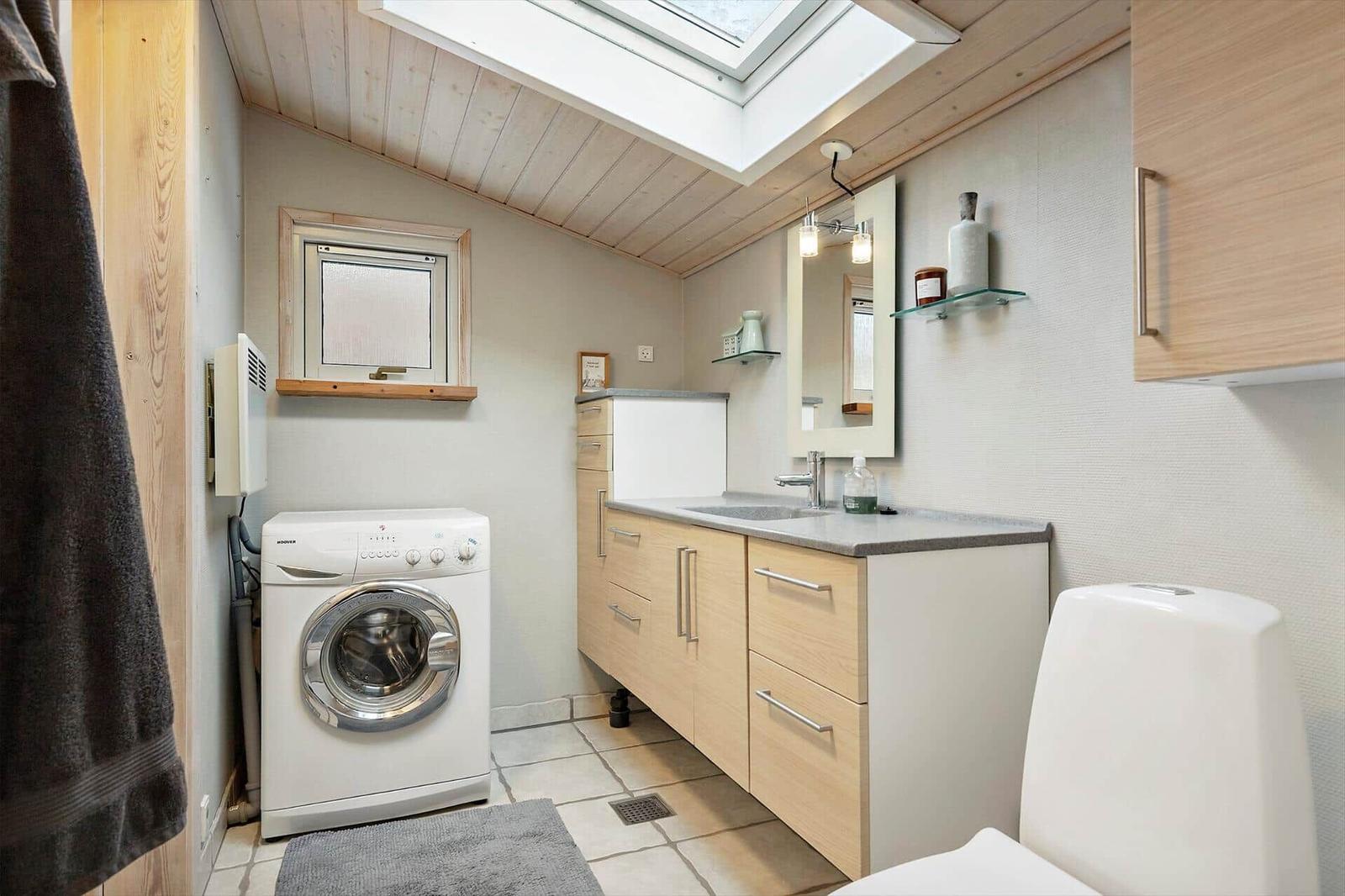 Bathroom with washing machine, sink, and toilet under skylight.