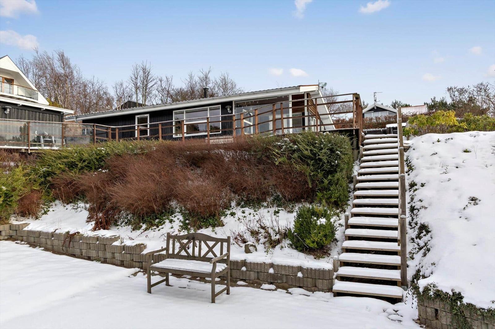 Snow-covered stairs lead to a house with a balcony and garden.