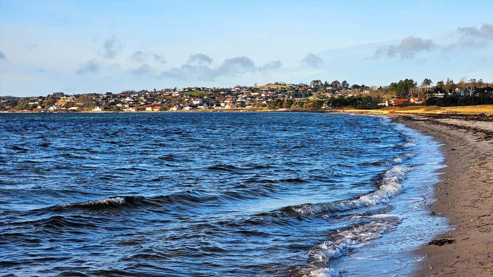 Beach with waves, view of inhabited hills in the background.