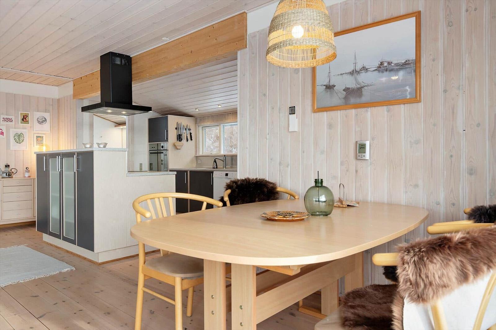 Dining area with wooden table and chairs. Kitchen in background. Wooden walls and ceiling.